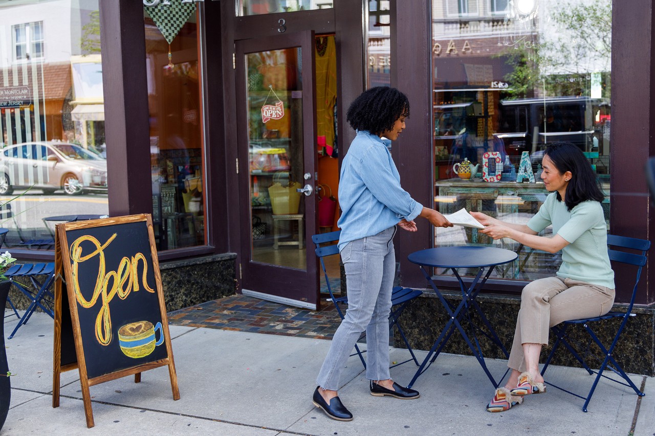 Woman hands customer a menu at outdoor café